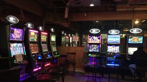 En rad spelautomater i ett svagt upplyst rum med träväggar och en bardisk i bakgrunden.
