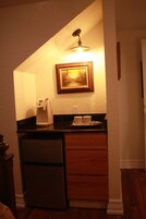 A compact kitchen with a coffee maker, a refrigerator, and a wooden cabinet.