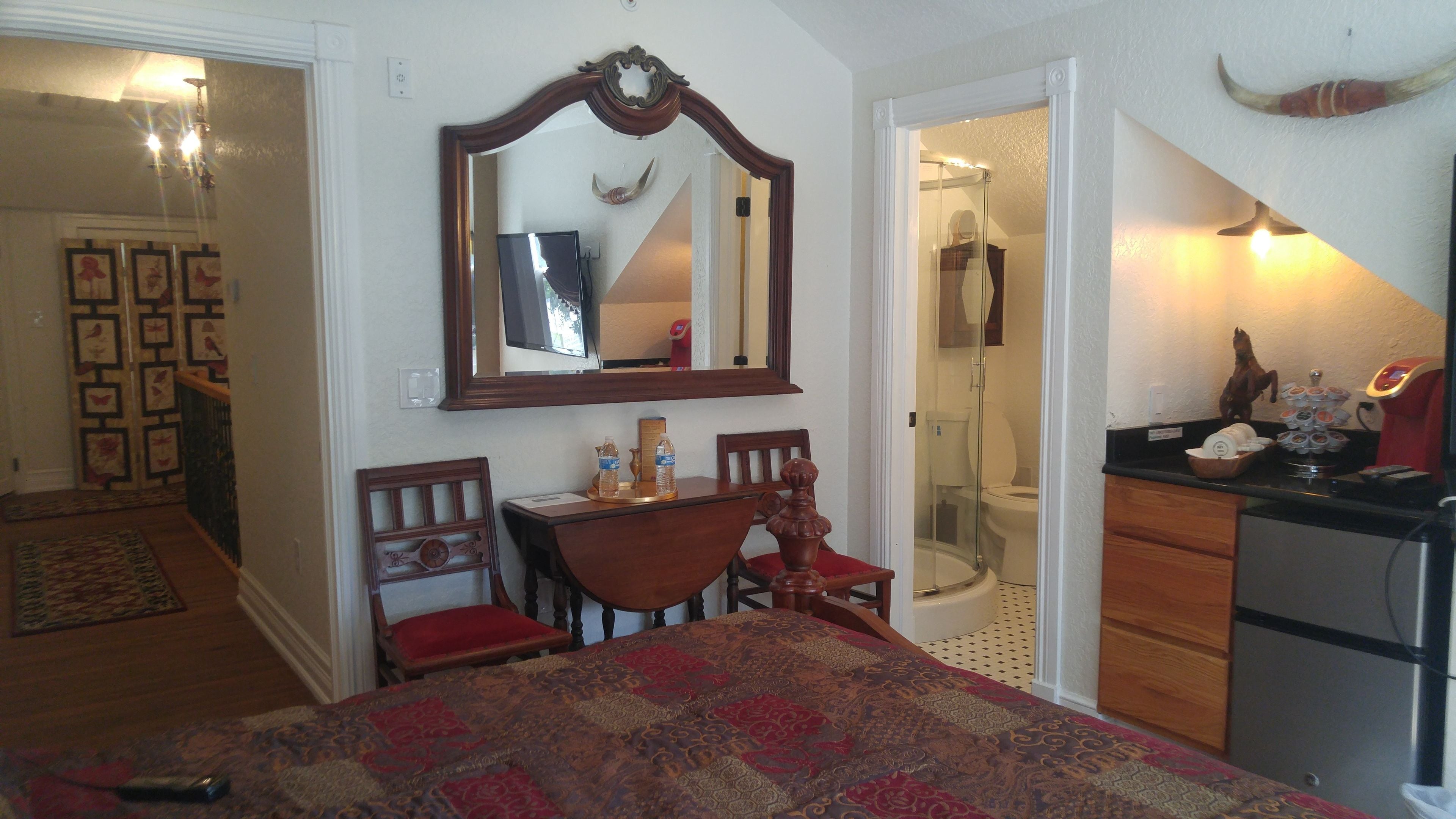 A bedroom with a bed, a desk, a chair, a mirror, a shower, and a bathroom.