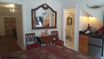 A bedroom with a bed, a desk, a chair, a mirror, a shower, and a bathroom.