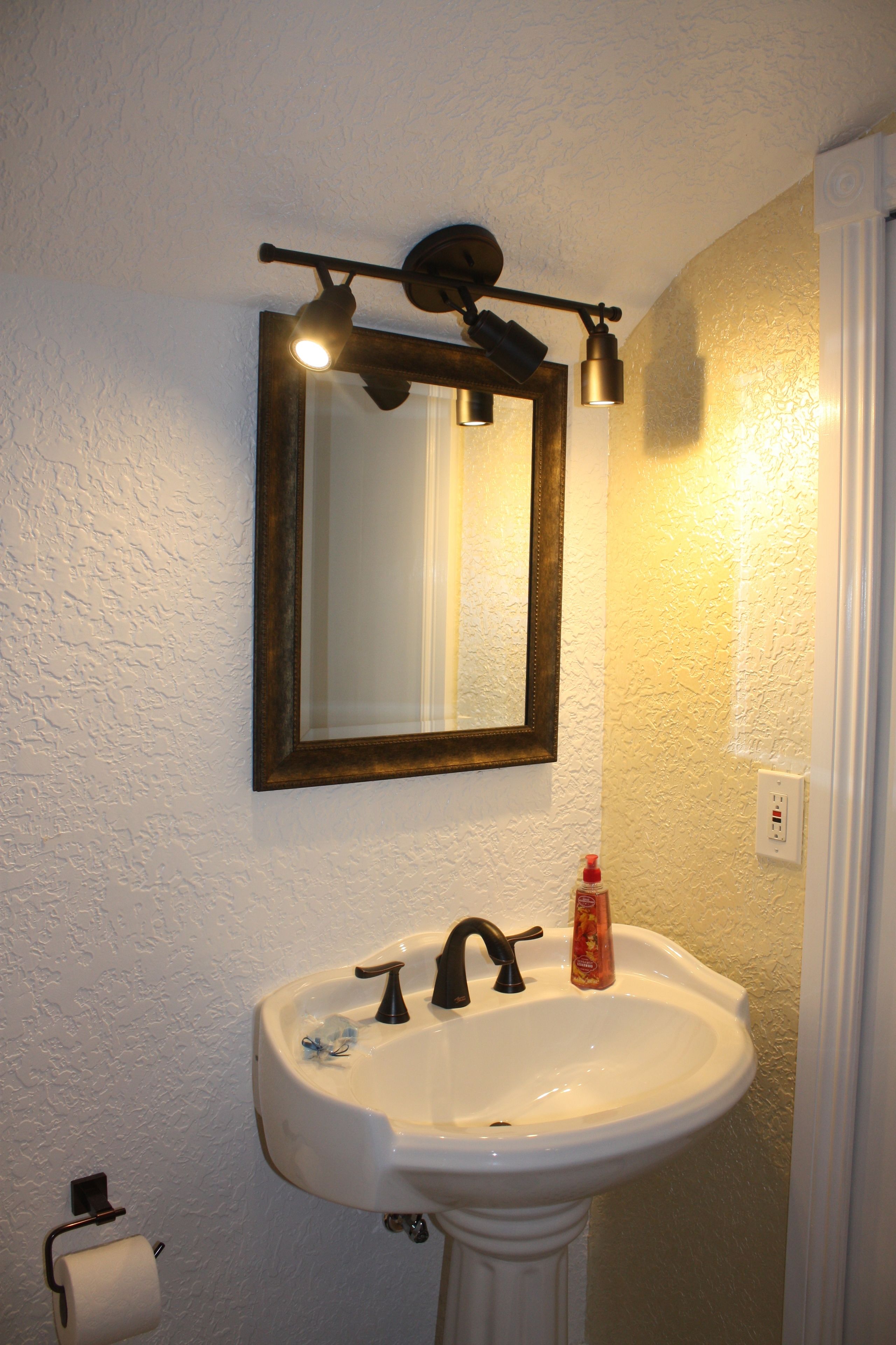 A bathroom with a white sink, a mirror, and a light fixture above the mirror.