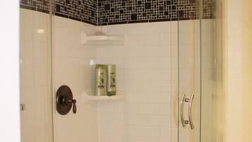 A glass-enclosed shower with a tiled floor and a shelf with toiletries.