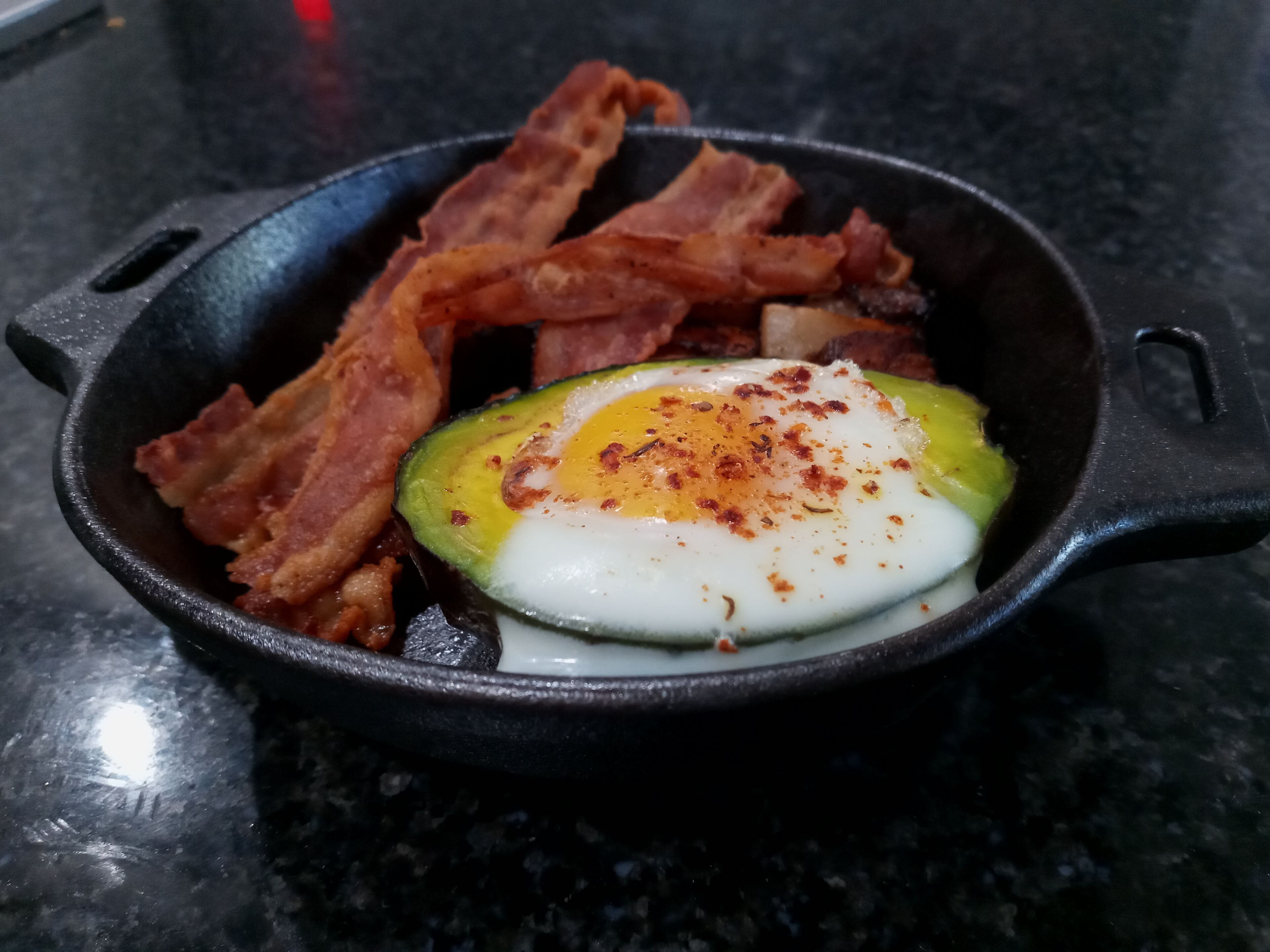 A cast iron skillet with bacon and a fried egg.