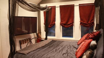 Un dormitorio con una cama grande, un televisor montado en la pared y una ventana con cortinas rojas.