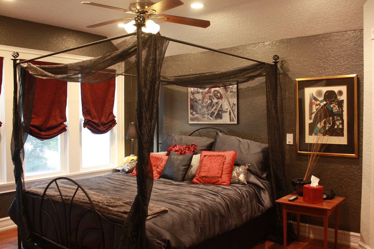 A four-poster bed with a canopy, a bedside table with a tissue box, and artwork on the walls.