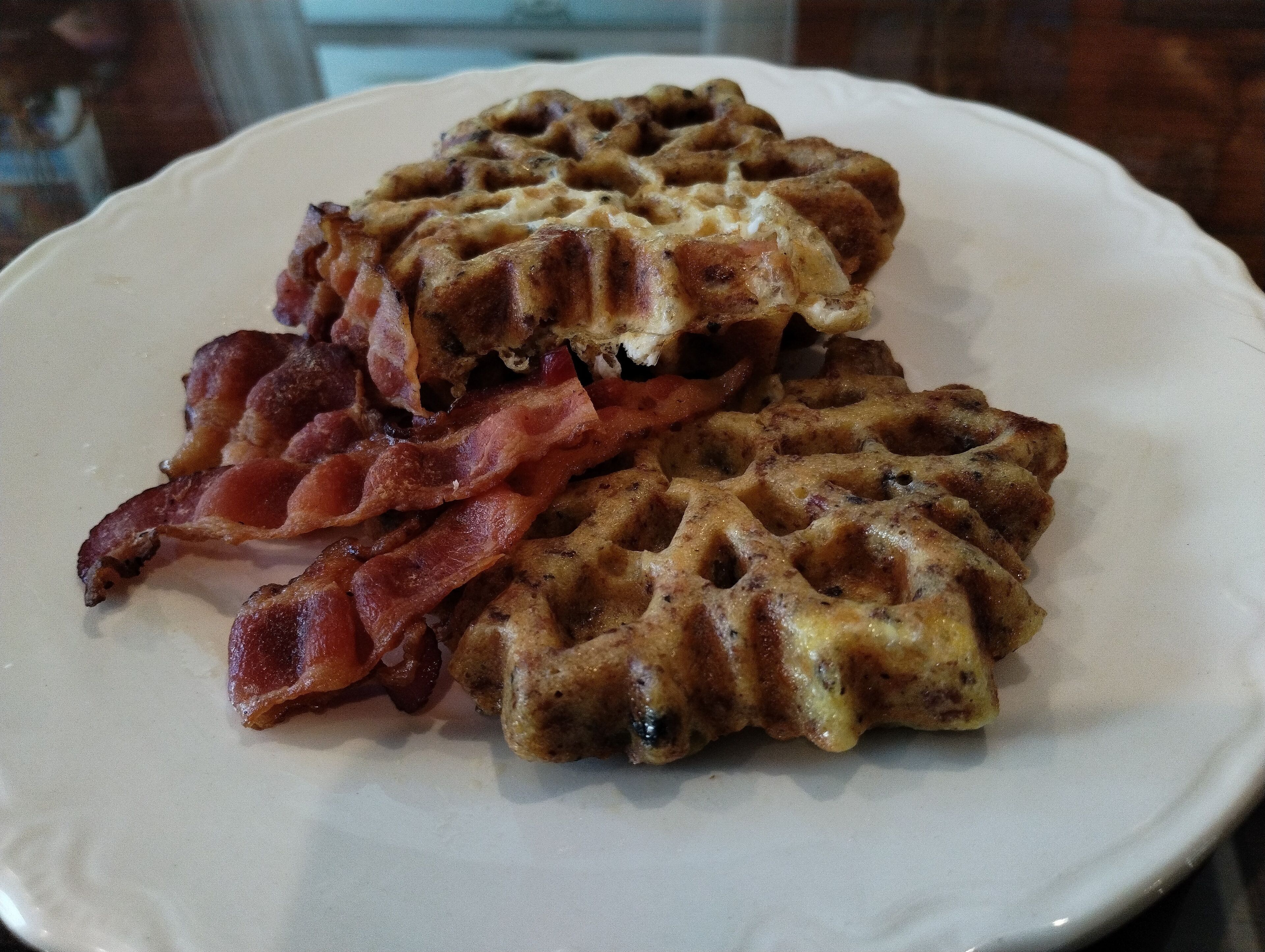 A plate with two waffles topped with melted cheese and strips of bacon.