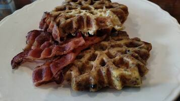 A plate with two waffles topped with melted cheese and strips of bacon.