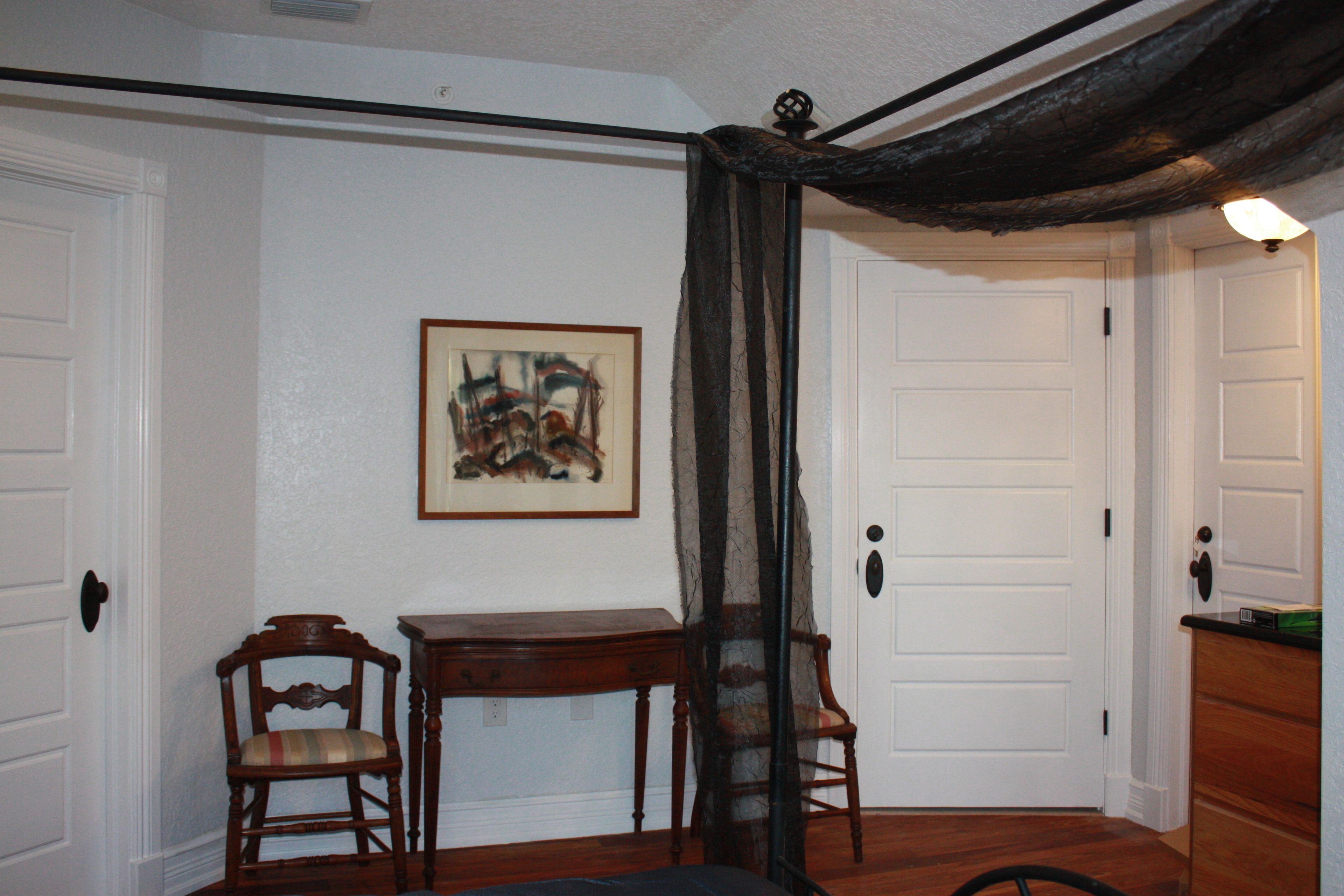 A room with a wooden table, two chairs, a framed picture on the wall, and a door with a light fixture above it.