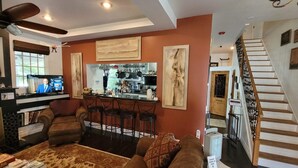 A living room with a sofa, chairs, a coffee table, a TV, and a kitchen in the background. - Kapp and Kappy B&B (Kissimmee)