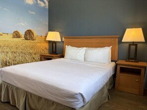 Un dormitorio con una cama, dos mesitas de noche con lámparas, un cabecero de madera y un mural de un campo en la pared.