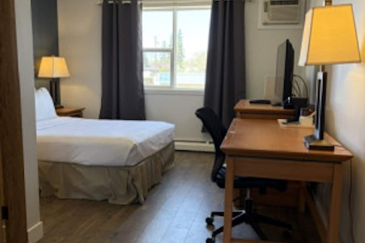 A hotel room with a bed, a desk, a chair, a television, and a window with curtains.
