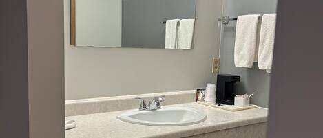 Une salle de bain équipée d’un lavabo, d’un miroir, d’un porte-serviettes et d’une poubelle.