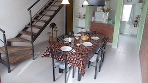 Uma sala de jantar com uma mesa posta para quatro pessoas, uma escada, uma televisão na parede e uma lareira de tijolos.
