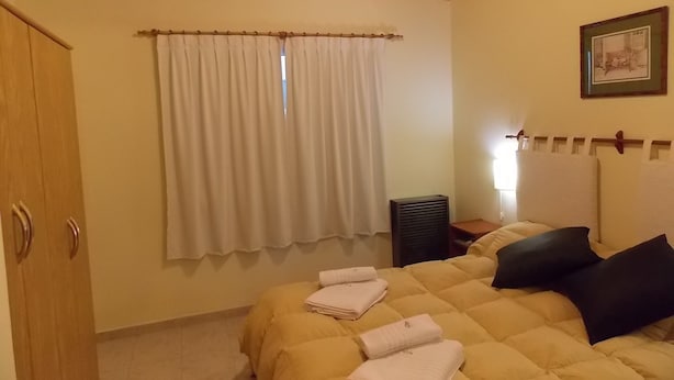 Quarto com teto de madeira, cama com edredom amarelo, toalhas brancas, mesa de cabeceira e um quadro emoldurado na parede.