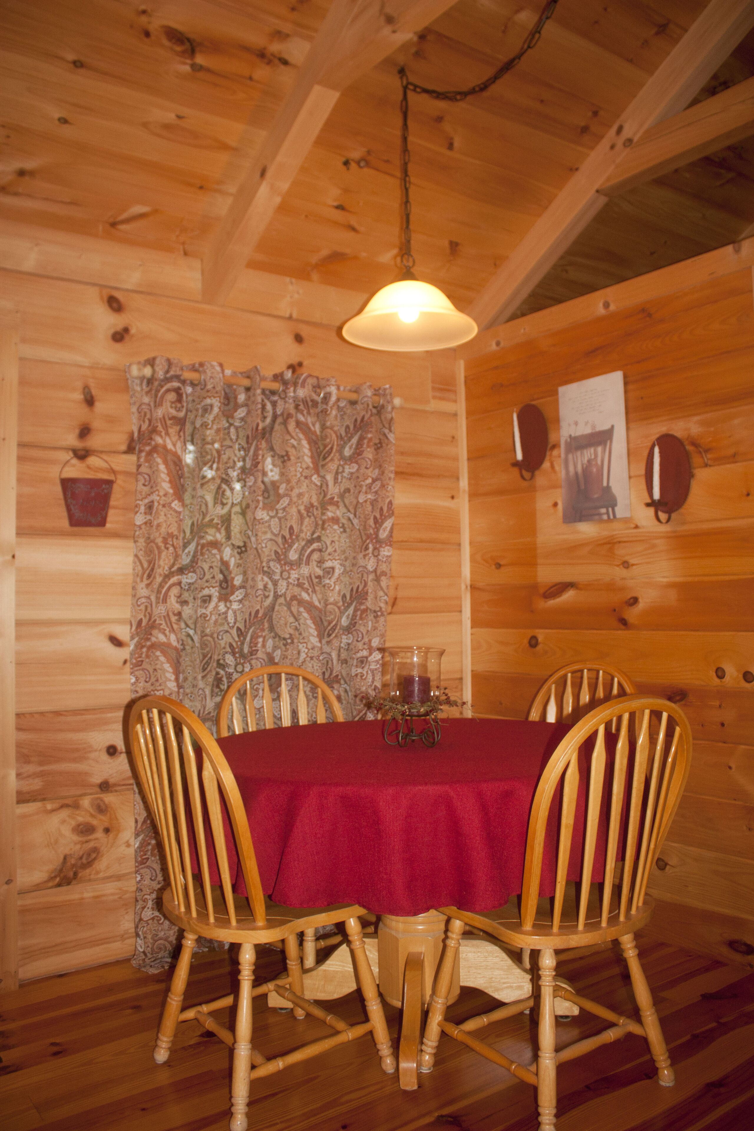 Une salle à manger en bois avec une table dressée pour quatre personnes, un luminaire suspendu et un rideau à motifs.