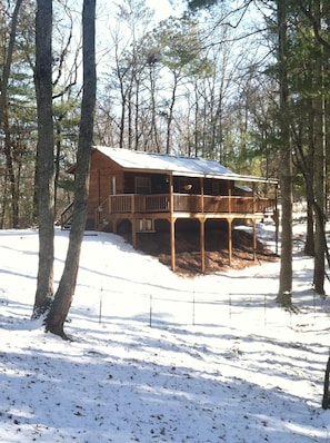 A cabin with a wooden deck, surrounded by trees and covered in snow.