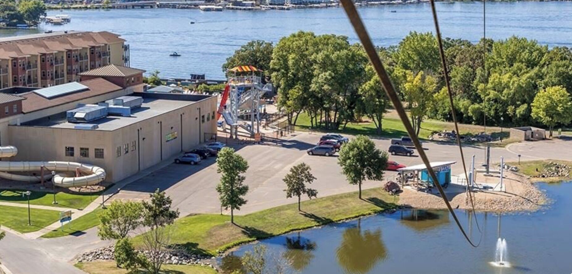 Vue aérienne d’un bâtiment avec un parking, un petit étang et des arbres.