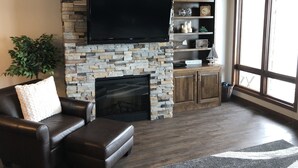 A living room with a stone fireplace, leather sofa, and a flat-screen TV mounted above it. - Great views! Third floor end unit - Indoor parking!  (Arnolds Park)