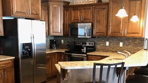 A modern kitchen with wooden cabinets, stainless steel appliances, a granite countertop, and a central island with bar stools. - Great views! Third floor end unit - Indoor parking!  (Arnolds Park)