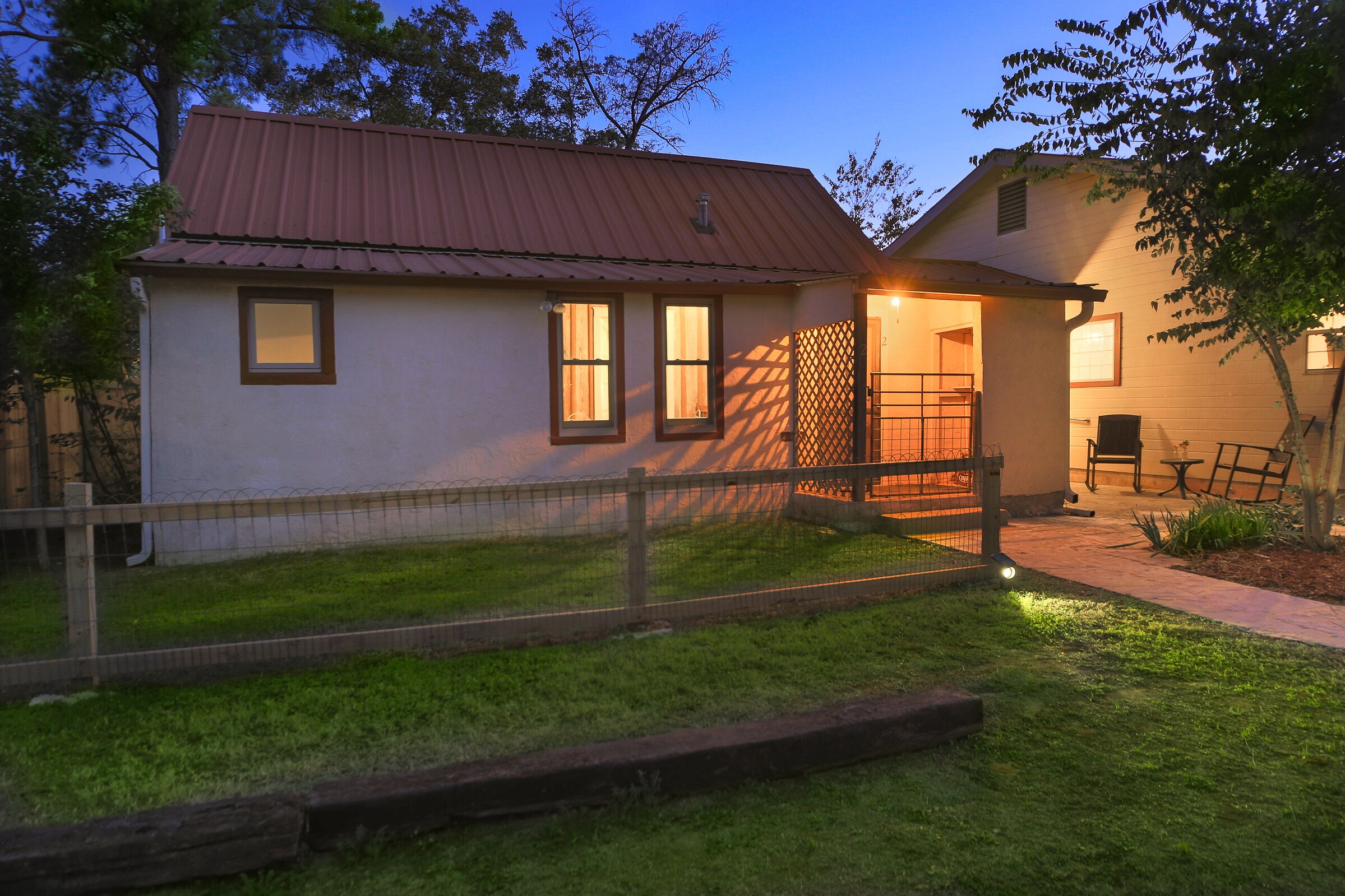 A two-story house with a red roof, a fenced yard, and a wooden deck.