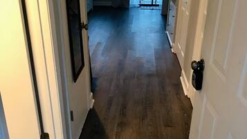 Un couloir avec un plancher en bois, des murs blancs et une porte sur le côté droit.
