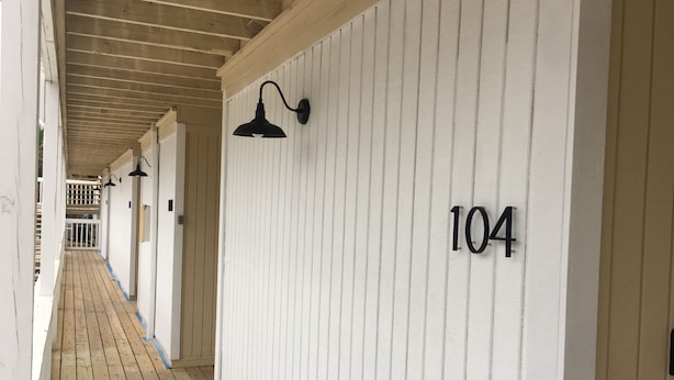 Ein Korridor mit Holzboden, weißen Wänden und schwarzen Wandleuchten. Die Nummer 104 ist an der Wand sichtbar.