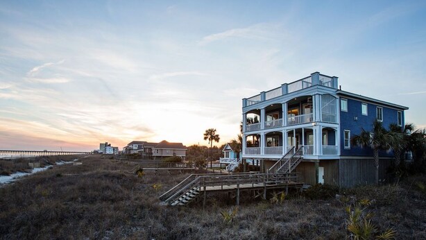 A coastal house with a wooden deck and stairs leading to a balcony.
