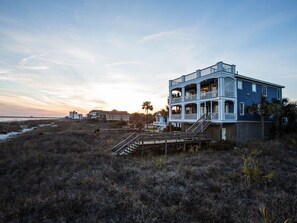Una casa costera con terraza de madera y escaleras que llevan a un balcón.