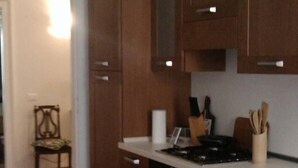 A modern kitchen with wooden cabinets, a white countertop, and a dining area with a table and chairs. - Spacious and bright apartment in Campo S.Alvise (Venezia)