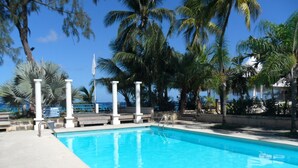 A clear blue pool with white columns and steps leading into it, surrounded by palm trees and a clear sky. - Only 3 mins walk to Beach and Beach Club (holetown)