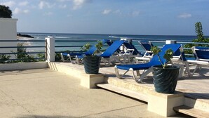 A rooftop lounge area with blue lounge chairs and potted plants, overlooking the ocean. - Only 3 mins walk to Beach and Beach Club (holetown)