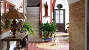 A hallway with a patterned floor, a wooden table with a lamp, potted plants, and a small dog. - Typical Andalusian House (sXVII) (Sanlúcar de Barrameda)