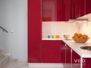 A modern kitchen with red cabinets, a white countertop, and a bowl of oranges. - 2 bedrooms, private terrace (Sevilla)