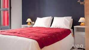 A bedroom with a bed, two bedside tables, a red blanket, white pillows, a yellow wall decoration, and a window with red curtains. - 2 bedrooms, private terrace (Sevilla)