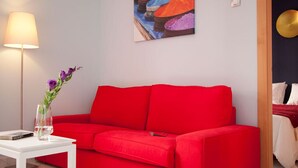 A red sofa, a white table, a vase with flowers, a lamp, and a colorful painting on the wall. - 2 bedrooms, private terrace (Sevilla)