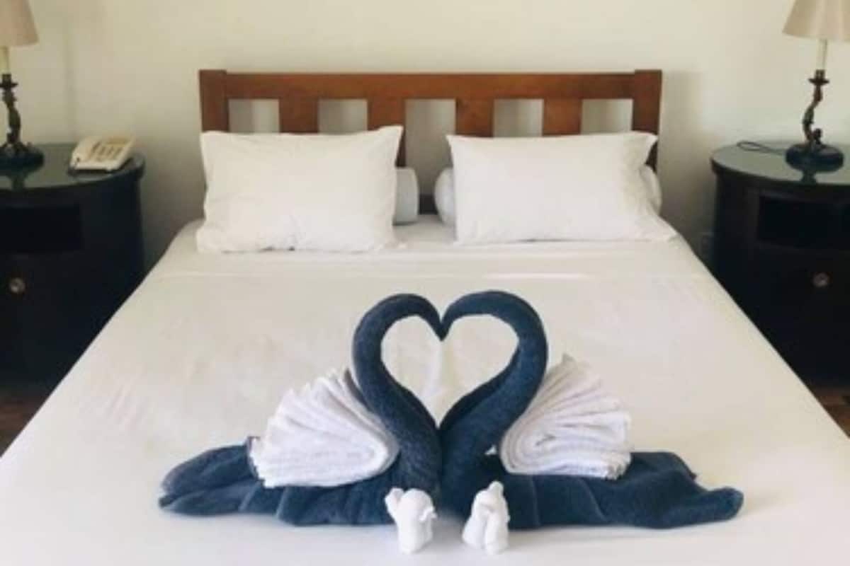Habitación de hotel con una cama grande, dos cuadros en la pared y una toalla con forma de corazón sobre la cama.