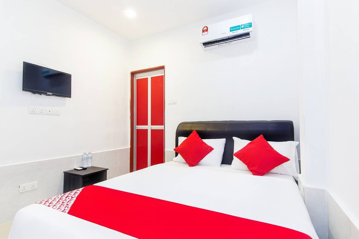 Ein Hotelzimmer mit einem Bett, einem an der Wand befestigten Fernseher, einer roten Tür und einer Klimaanlage.