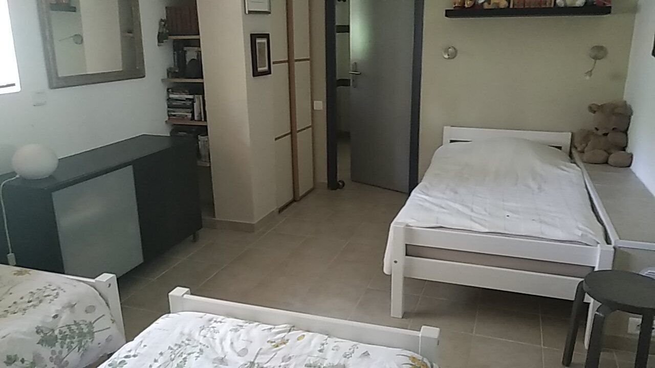 Un dormitorio con cama, mesita de noche y un osito de peluche en un estante.