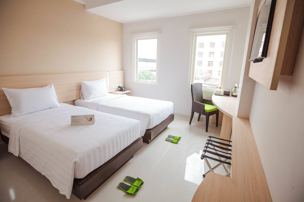 Habitación de hotel con dos camas, un escritorio, una silla y un ventanal.