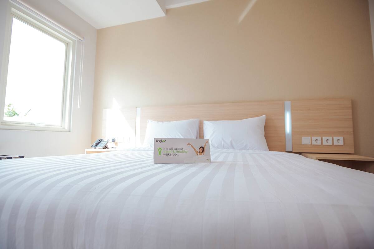 Una habitación de hotel con una cama grande, una mesita de noche con teléfono y una ventana con persianas.