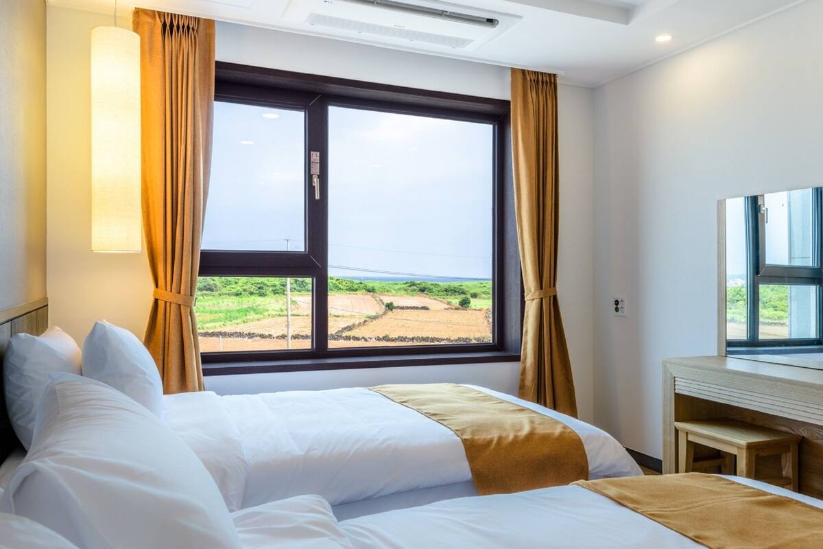 A hotel room with a large window, two beds, a desk, and a view of a landscape.