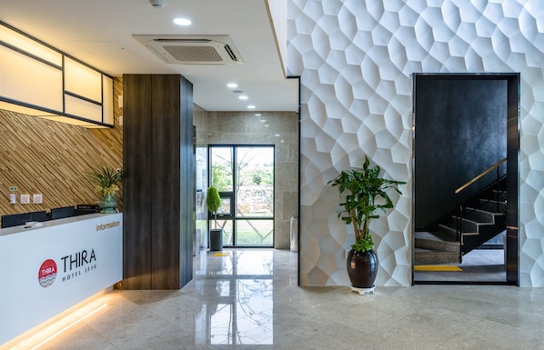 A modern hotel reception area with a reception desk, a staircase, and a large window.