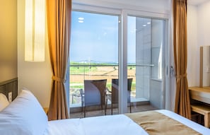 A hotel room with a bed, a chair, and a view of a green landscape through a glass door.