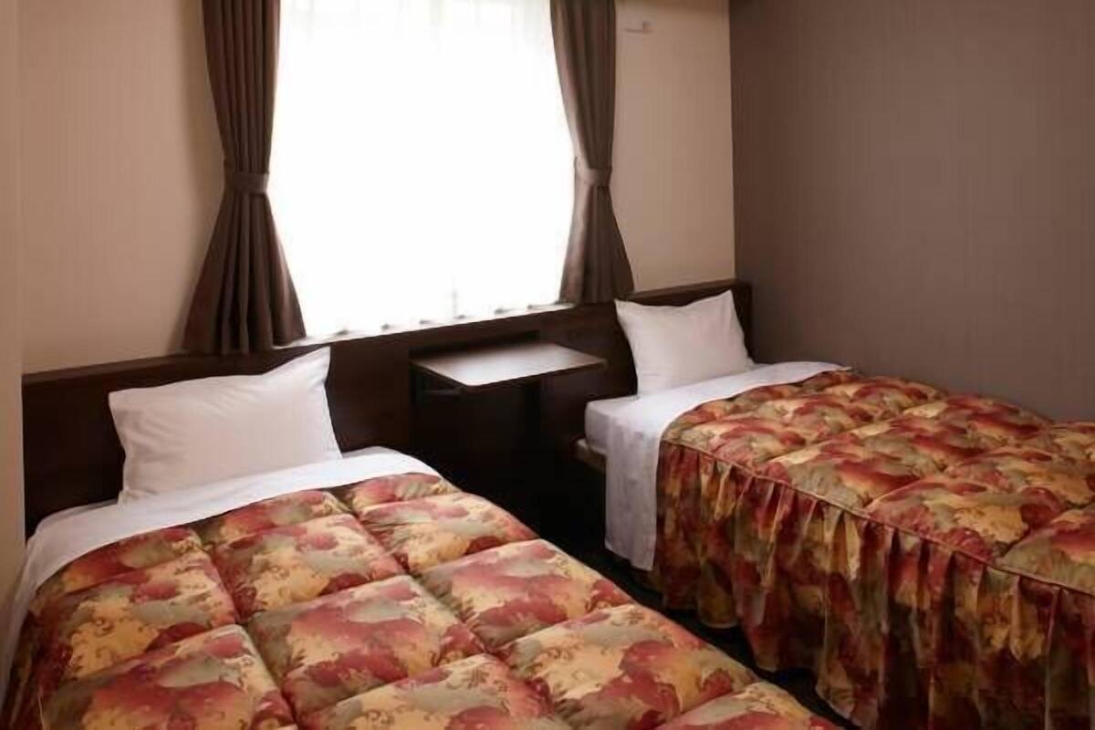 A hotel room with two beds, a small desk, and a window with curtains.