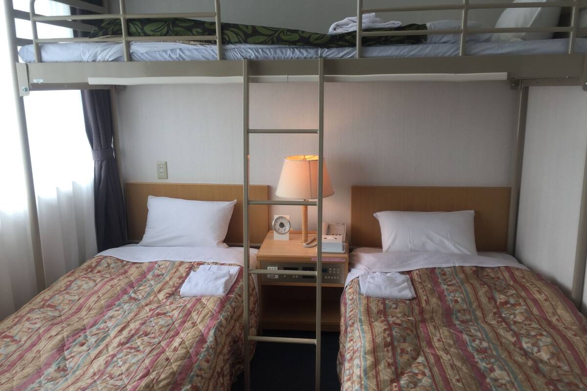 A bunk bed room with two beds, a nightstand with a lamp, and a window with curtains.