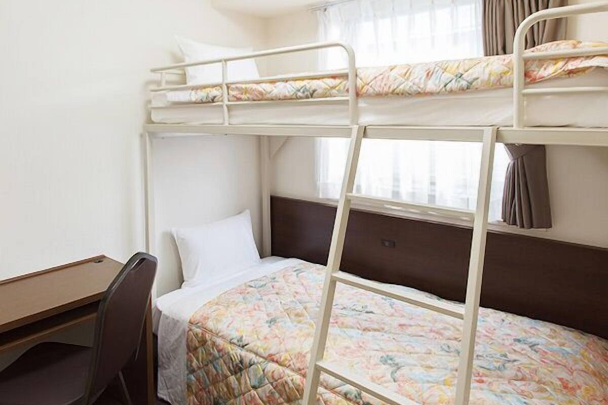 A bunk bed room with a desk and chair, a window with curtains, and a ceiling light.