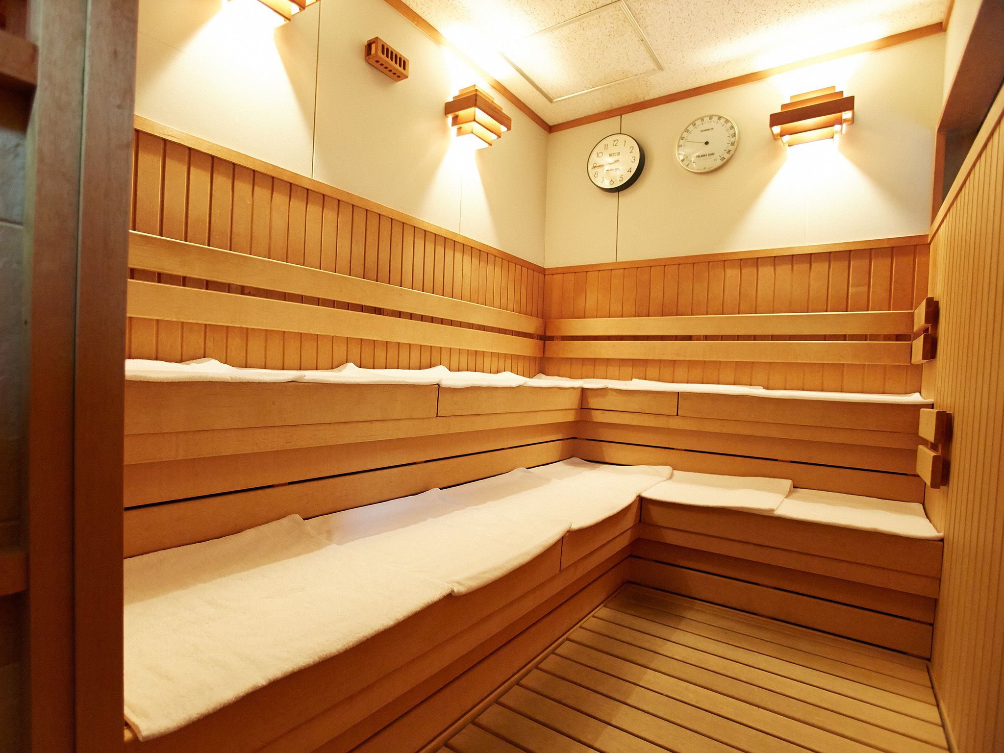 A sauna with wooden benches and two wall-mounted clocks.