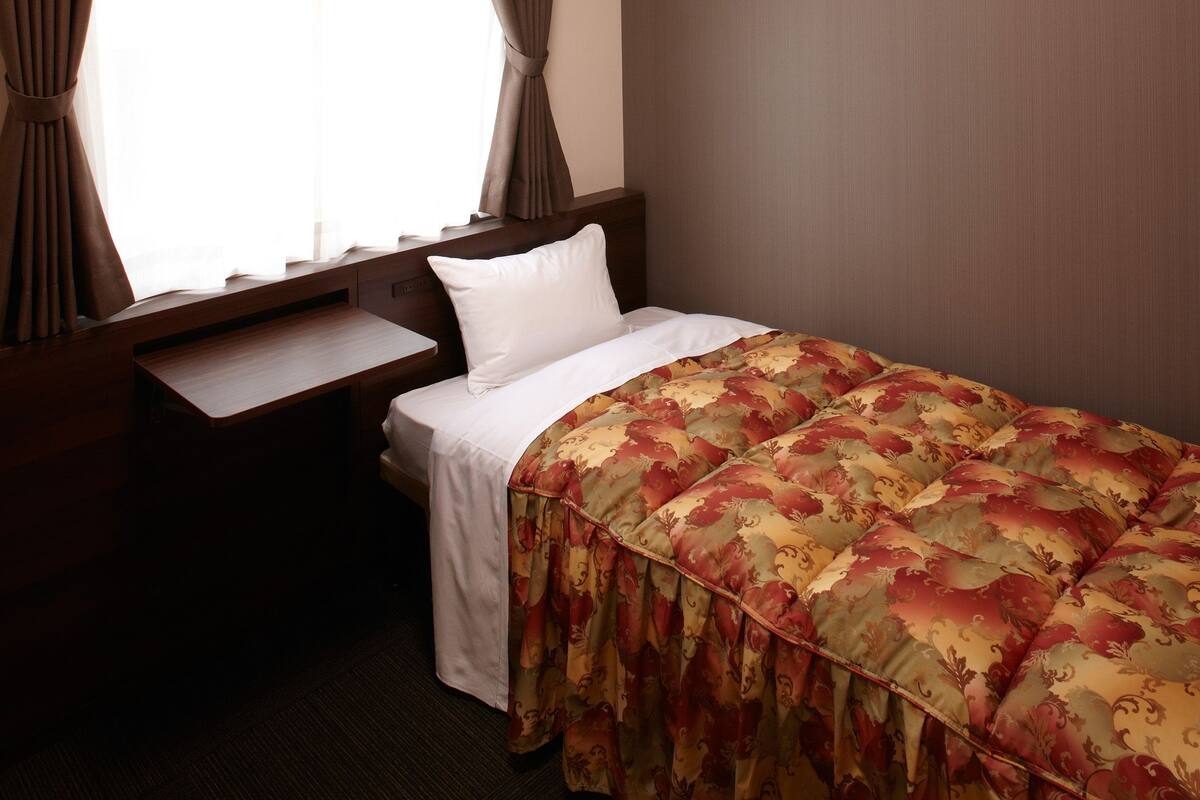 A hotel room with a bed, a small desk, and curtains.