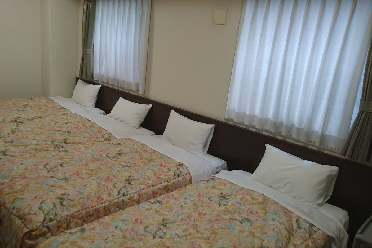 A hotel room with two beds, each with floral-patterned bedding, white pillows, and a wooden headboard.