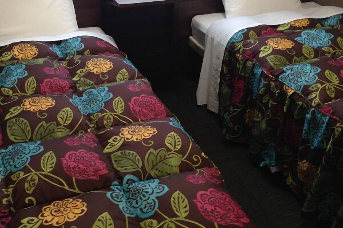 A hotel room with two single beds, a small table, and a window with curtains.